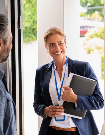 Smiling mature social counselor meeting mature couple at home. Happy multiethnic man and latin woman greeting agent at home standing near door. Successful social worker consultant on the doorstep meeting ethnic couple.