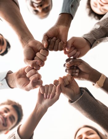 Teamwork, Power And Partnership Concept. Below view of multucultural group of smiling people making fist bump standing in circle. Workers doing fist pump together celebrating good deal